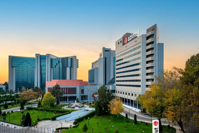 The facade and entrance area of AZIMUT Grand Hotel Tashkent, viewed across the garden