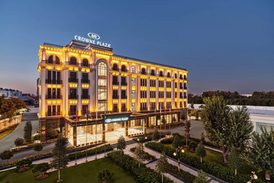 Crowne Plaza Tashkent lit at dusk, seen from its garden
